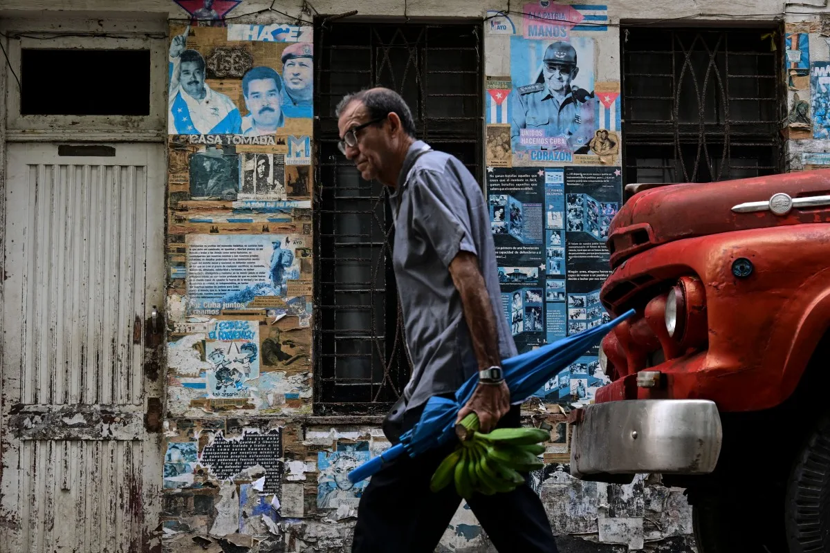 Um homem carregando bananas e um guarda-chuva dobrado passa por cartazes que retratam o presidente venezuelano Nicolás Maduro, o ex-presidente venezuelano Hugo Chávez