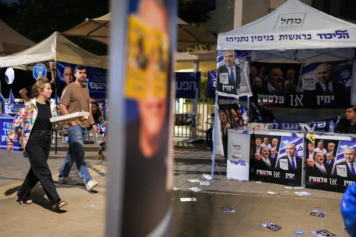 Pessoas passam por estandes de campanha do partido Yashar (à esquerda) e do partido Likud do lado de fora de um local de votação em Tel Aviv. 27/10/2026.