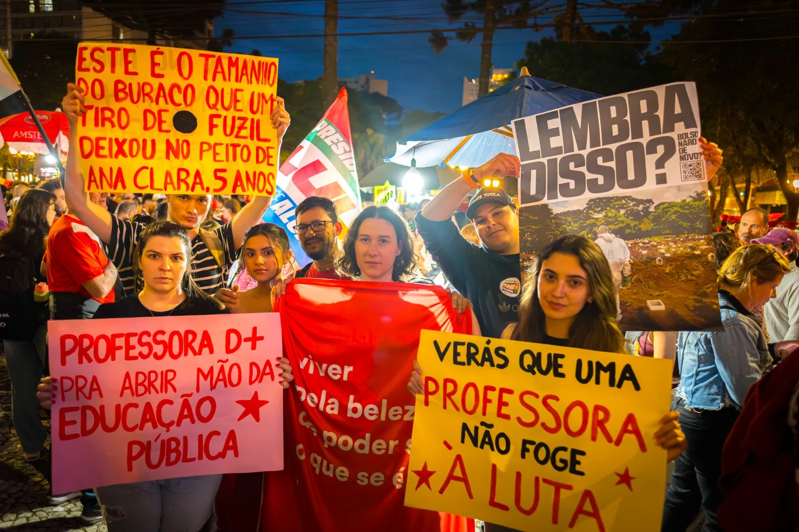 Imagem mostra professoras e estudantes segurando cartazes com críticas a Flávio Bolsonaro