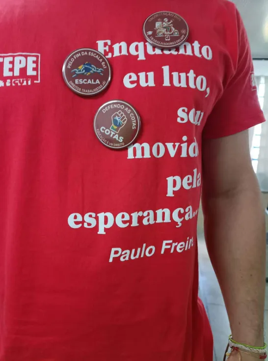 Professores usavam camisas vermelhas, mesma cor do fardamento escolar, com frase de Paulo Freire e broches a favor de cotas, valorização dos trabalhadores de apps e contra a escala 6x1, mas sem qualquer conotação partidária ou eleitoral