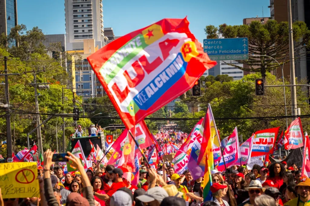 Imagem mostra multidão participando do ato, com uma bandeira de Lula balançando ao vento