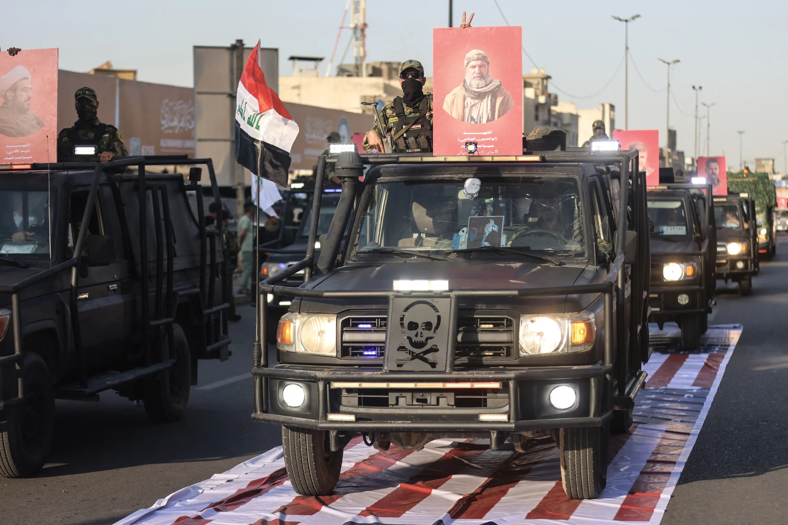 Members of the Hashed al-Shaabi forces carry portraits as they drive over a US flag during a symbolic funeral procession honouring those killed in US-Israeli attacks and celebrating the withdrawal of the US-led coalition from Iraq, in Baghdad on October 1, 2026. The US-led, anti-jihadist coalition officially ended its mission in Iraq on September 30, more than a decade after it deployed to the country to help fight the Islamic State (IS) group. (Photo by AHMAD AL-RUBAYE / AFP)
