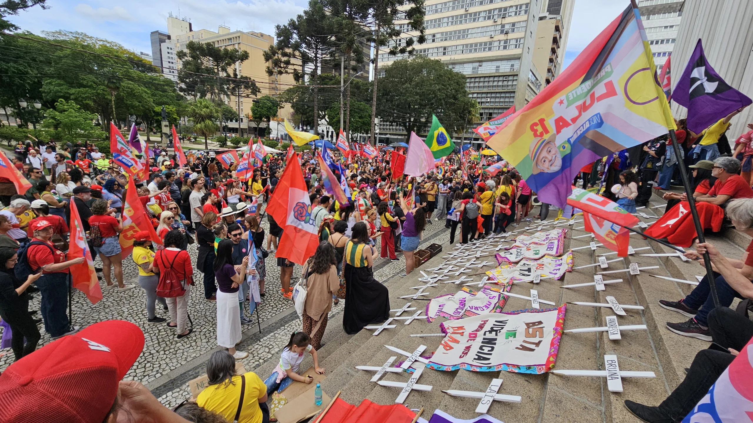 Imagem mostra uma concentração de mulheres em frente ao prédio histórico da Praça Santos Andrade. No chão, algumas cruzes representam as vítimas de feminicídio