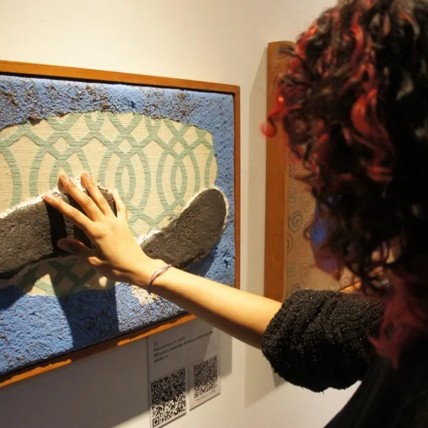 Visitante explora as texturas e os relevos de uma das obras da exposição tátil Sob os Pés do Mundo: Arte e Inclusão, que propõe novas formas de experimentar a arte por meio do toque